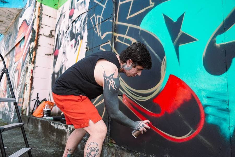 Riverón spraying red paint on a wall piece