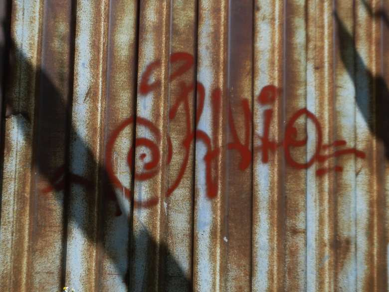 Red handstyle tag sprayed on rusted corrugated steel